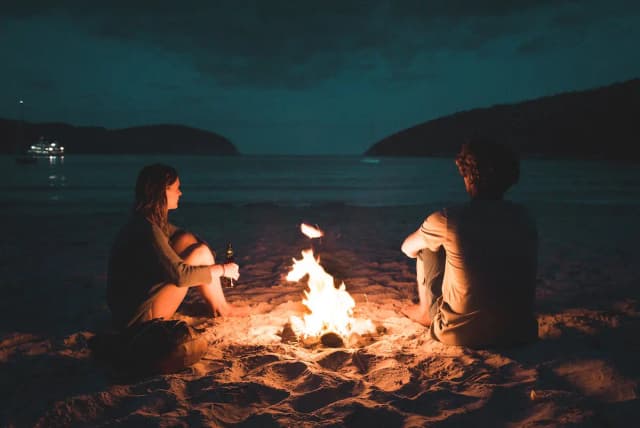 a couple sitting around a fire on a beach at night