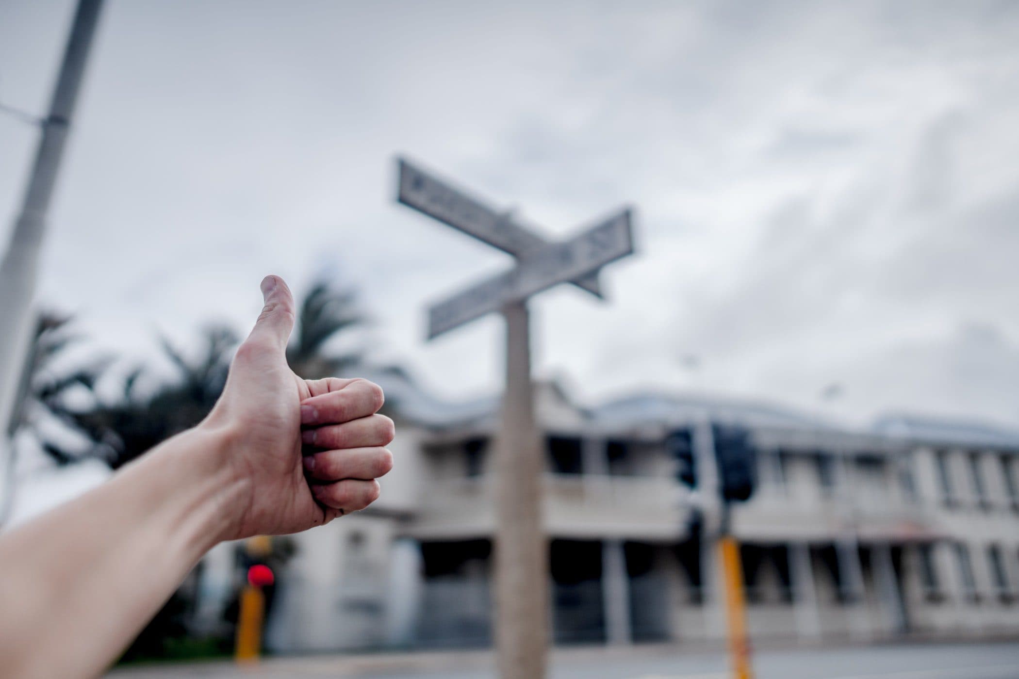 a hand giving a thumbs up in front of a street sign