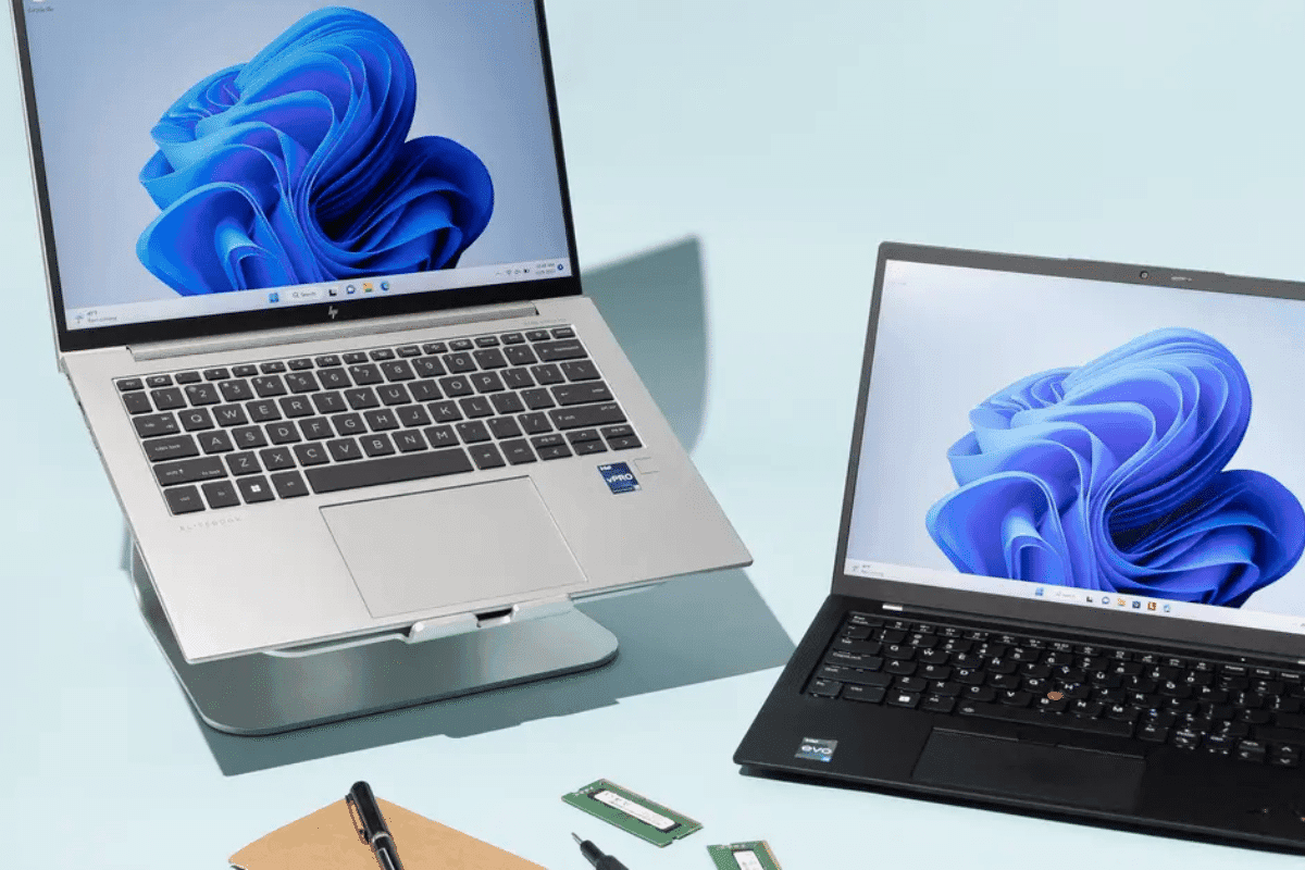 Two laptops, a pen, and a notebook are placed on a table, creating a productive workspace for digital and handwritten tasks