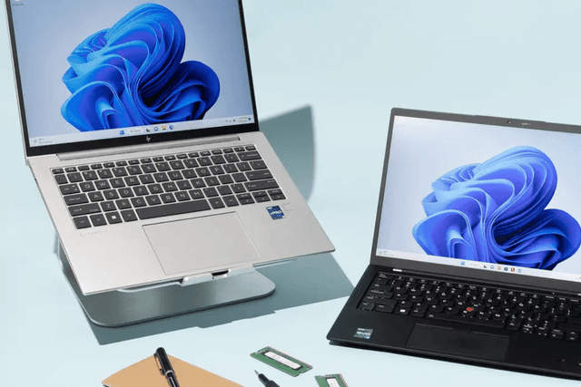 Two laptops, a pen, and a notebook are placed on a table, creating a productive workspace for digital and handwritten tasks