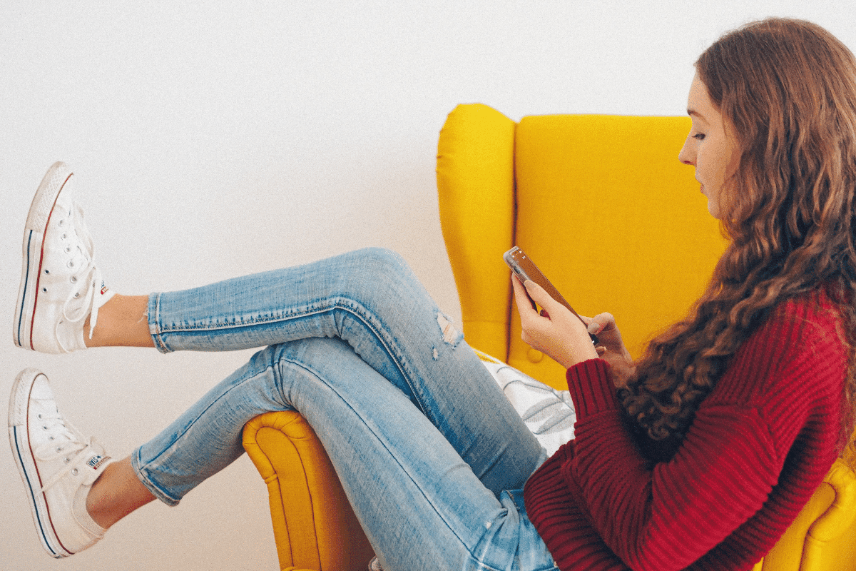 a person sitting in a yellow chair looking at her phone