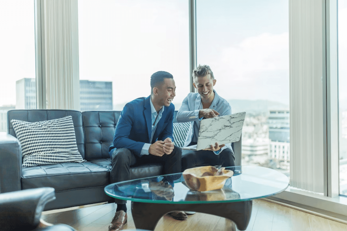 two men sitting on a couch looking at a laptop