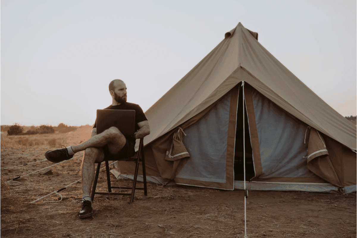 a person sitting in a chair with a laptop in front of a tent