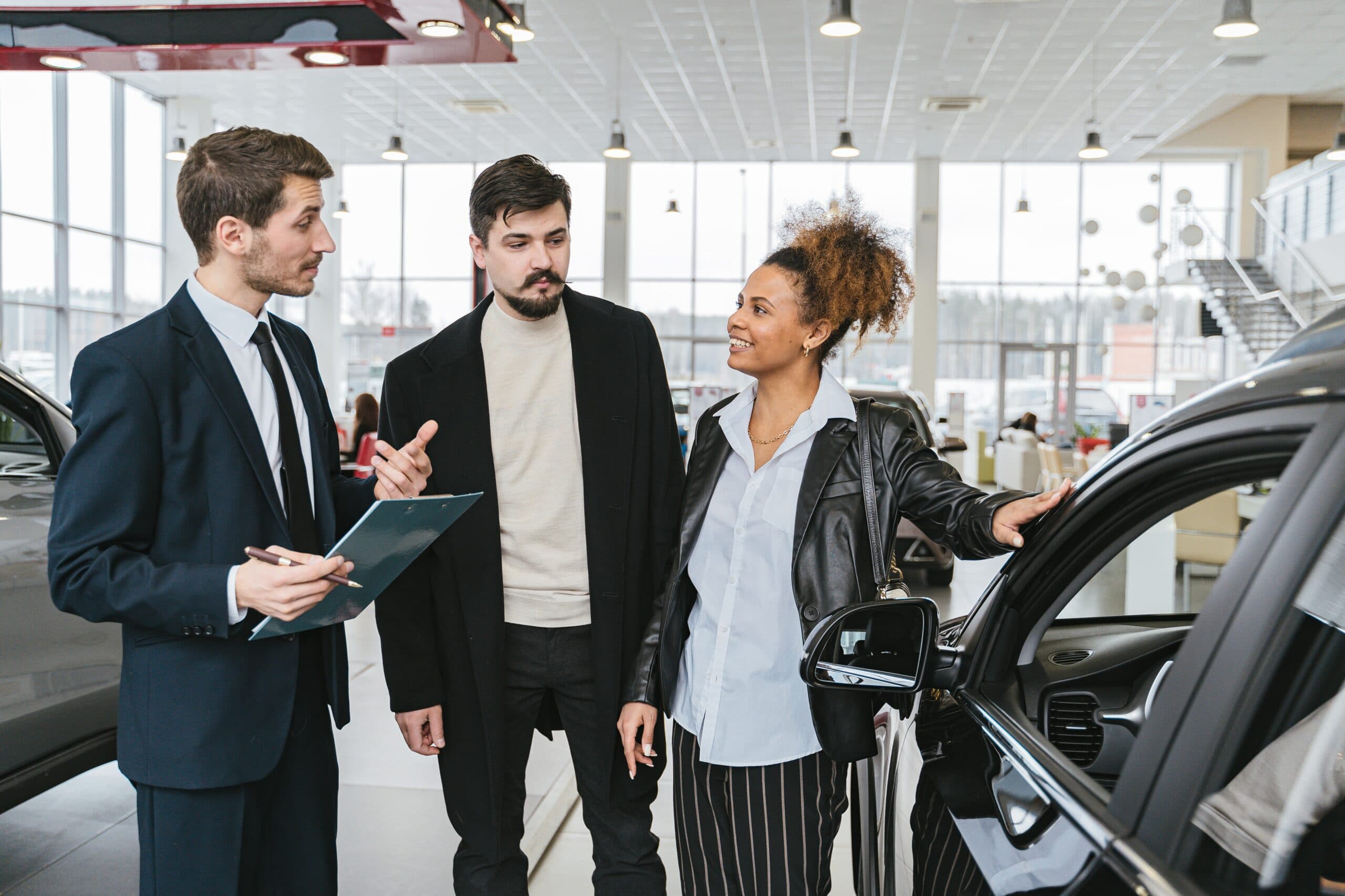 Two individuals and a lady inside an automobile dealership.