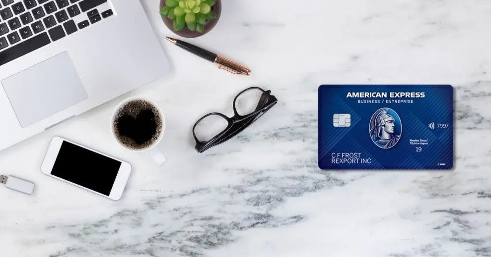 a credit card of American Express Company with glasses, cellphone, a pen, laptop and a cup of coffee