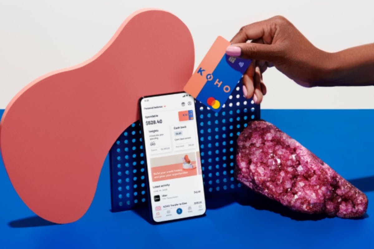 a hand holding a credit card and a phone next to a pink object
