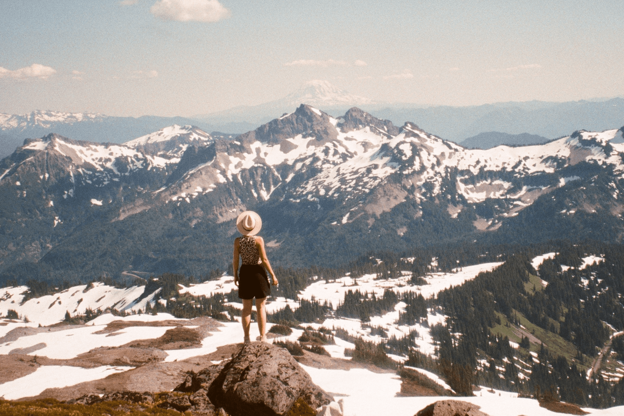 Woman standing on mountain peak, admiring snow-capped peaks in the distance.