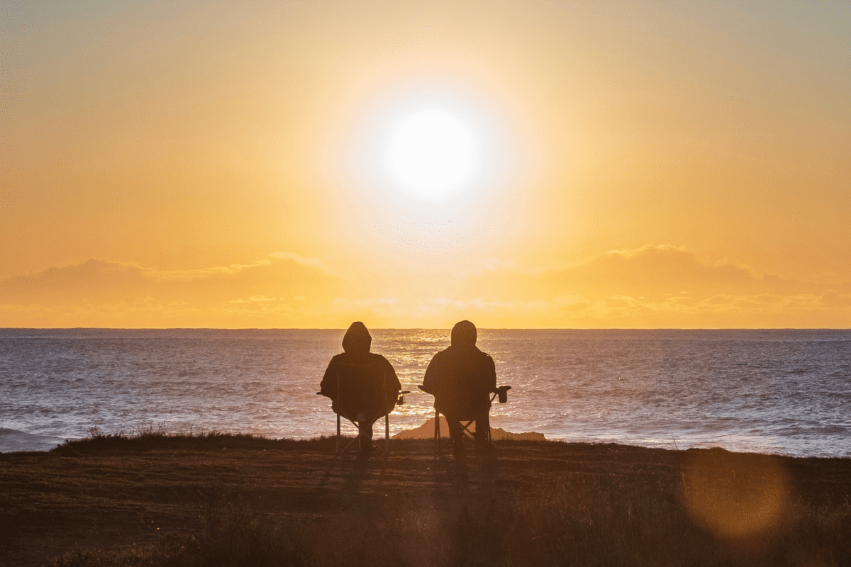 Two individuals siton chairs, gazing at the ocean during a breathtaking sunset.