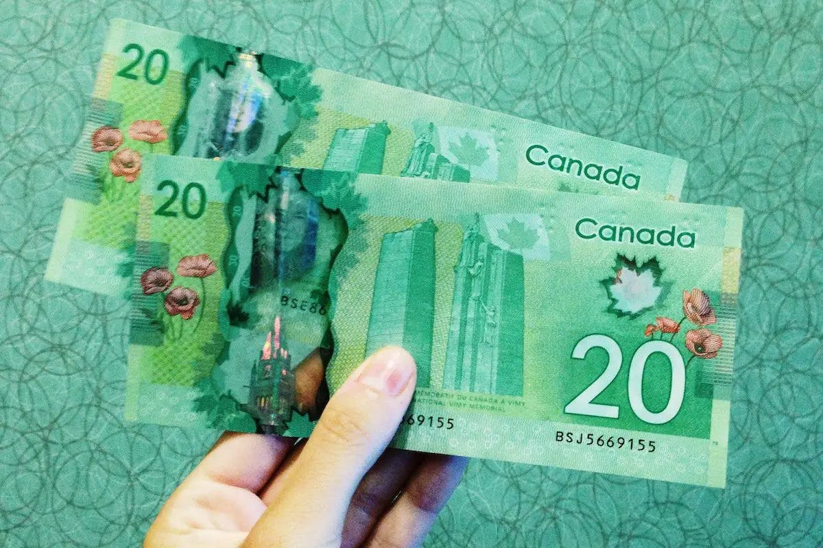 Two Canadian dollars held up against a green background, showcasing the currency's design and value.