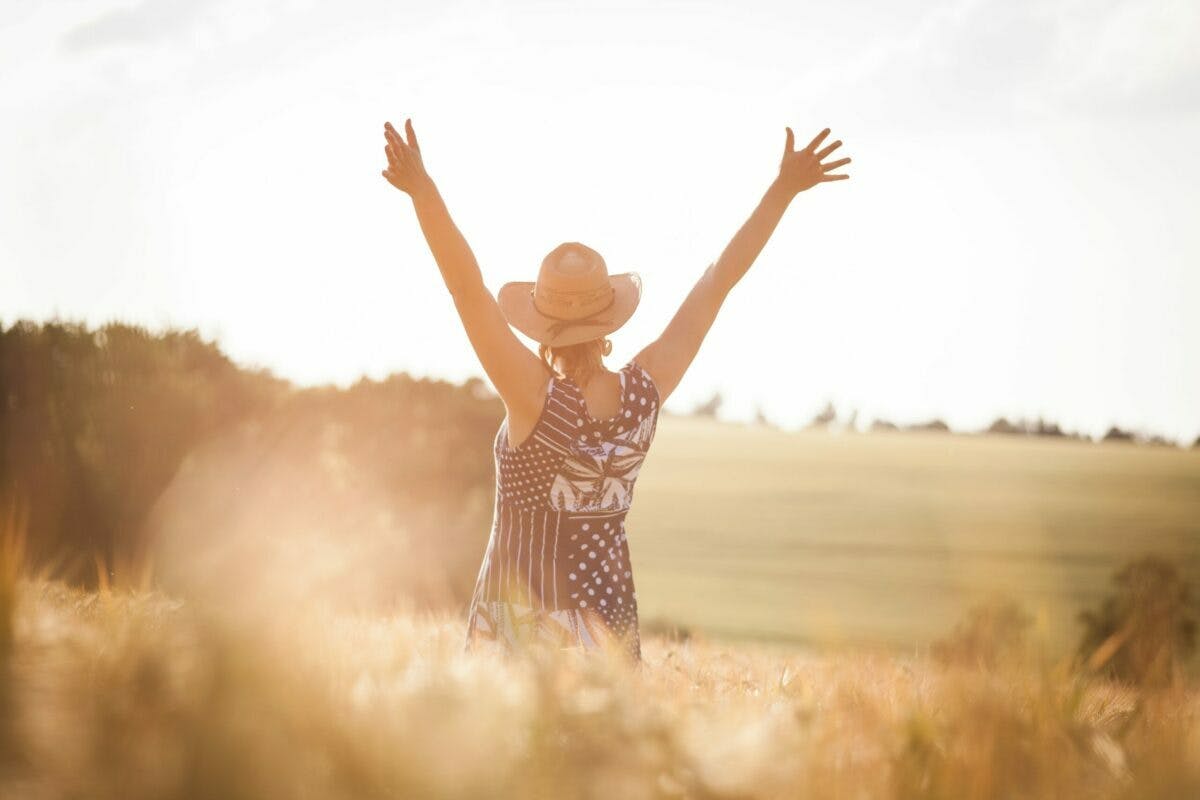a woman in a hat with her arms raised in a field