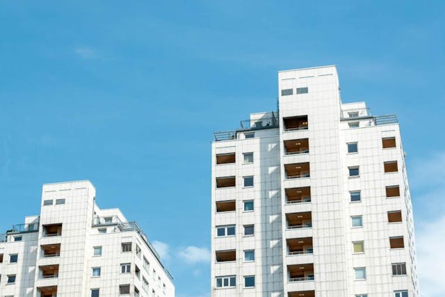 Two towering white buildings adorned with balconies, set against a serene blue sky.
