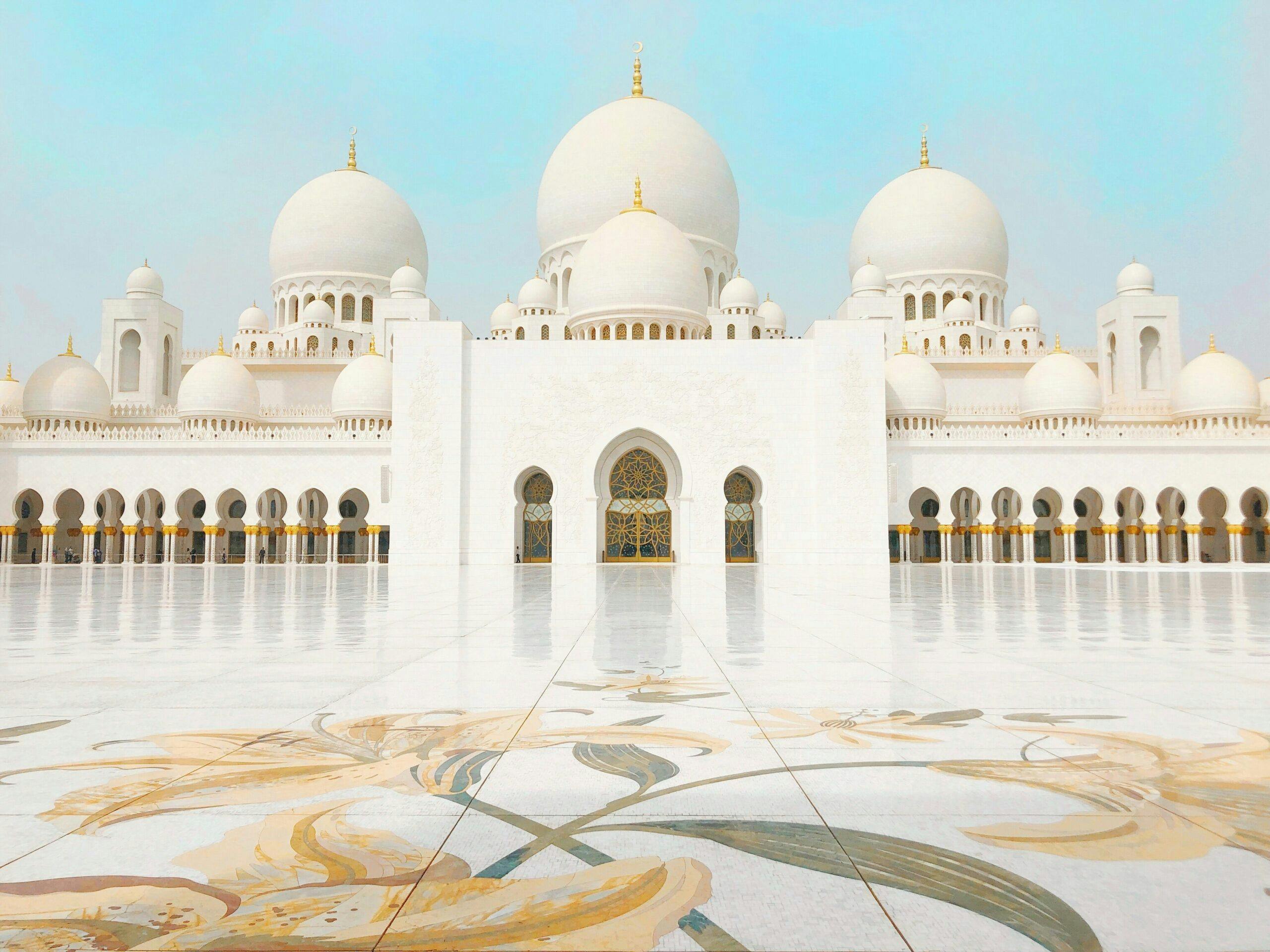 a large white building with domes and a tiled floor with Sheikh Zayed Mosque in the background