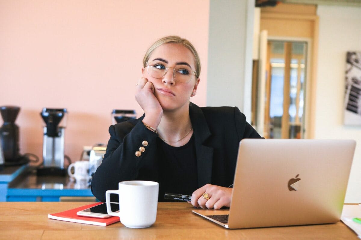 a woman sitting in a stress mood at a table with a laptop and a cup