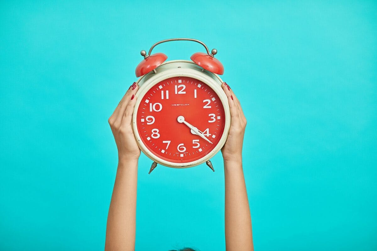 A women holding up an alarm clock against a blue background, symbolizing punctuality and time management