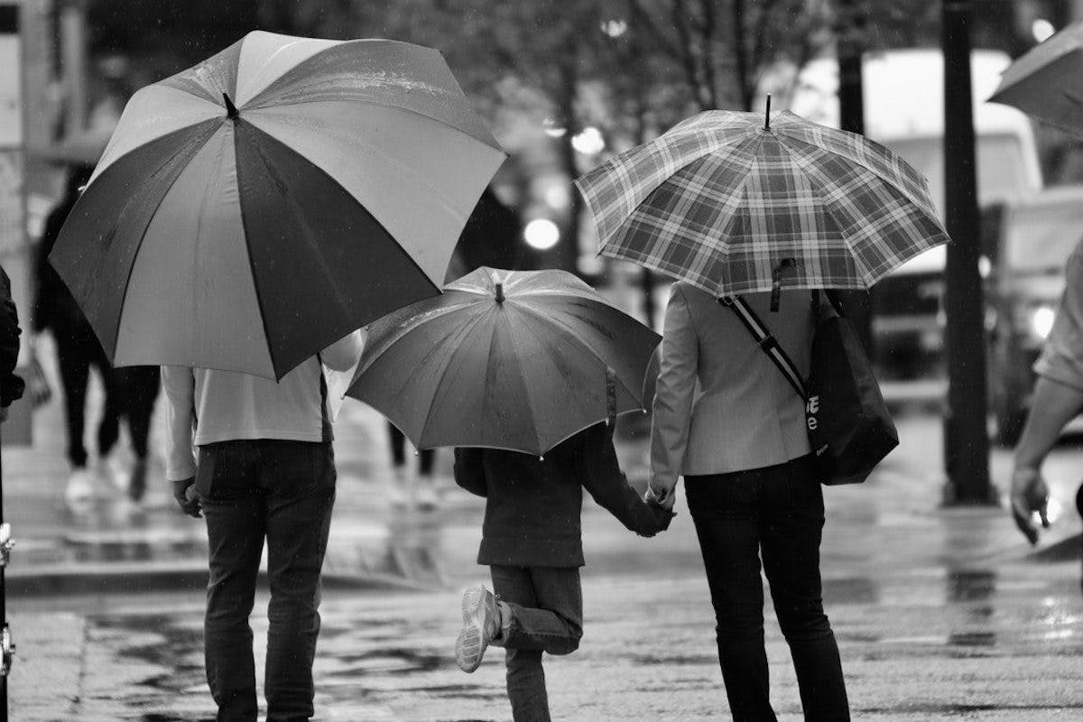 Three individuals holding umbrellas in a black and white photograph.
