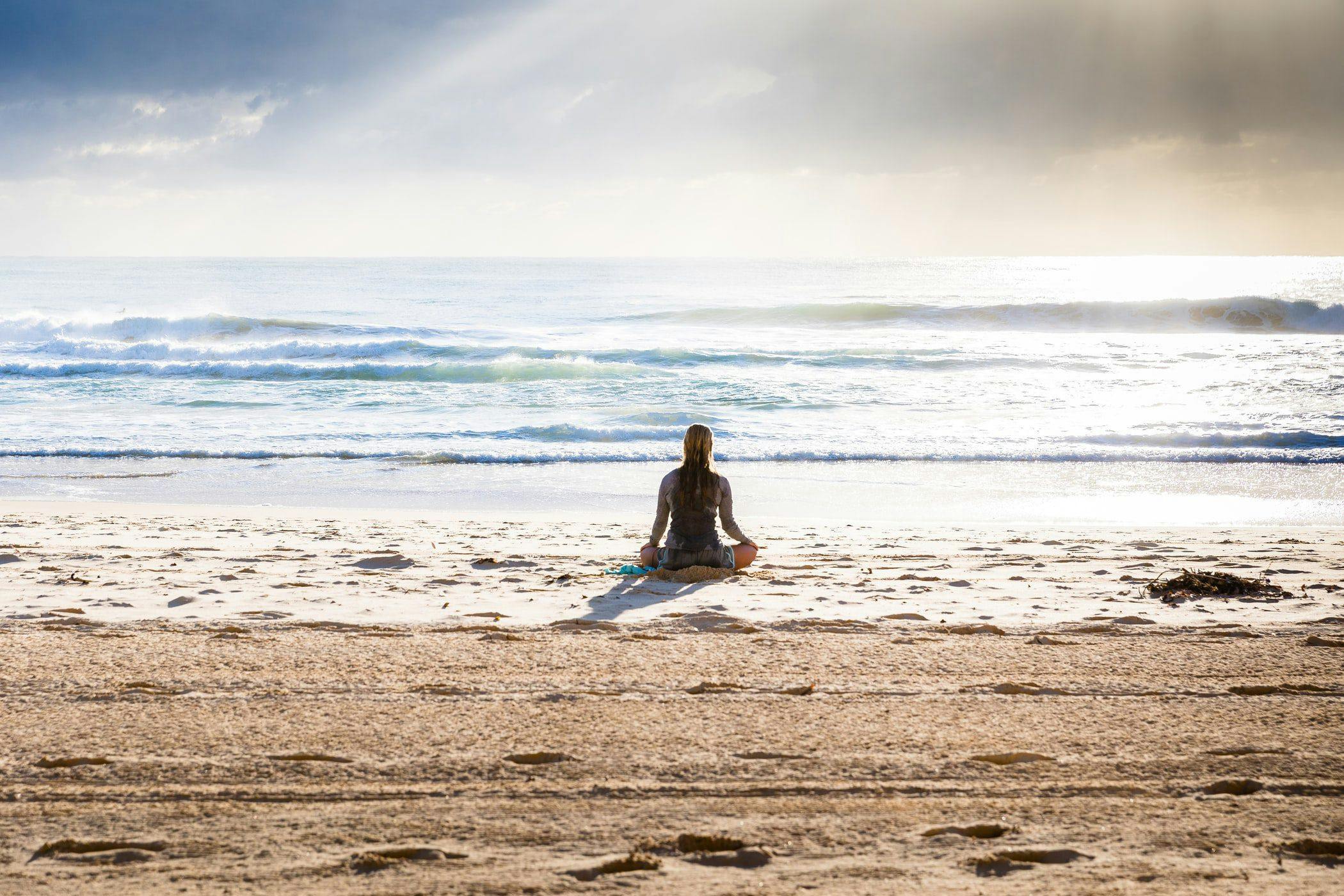 Serene woman in meditation pose on beach with ocean view