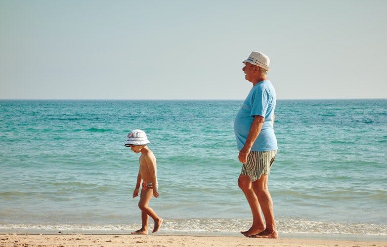 An elderly man and a young boy strolling along the sandy beach, enjoying a serene moment by the sea.