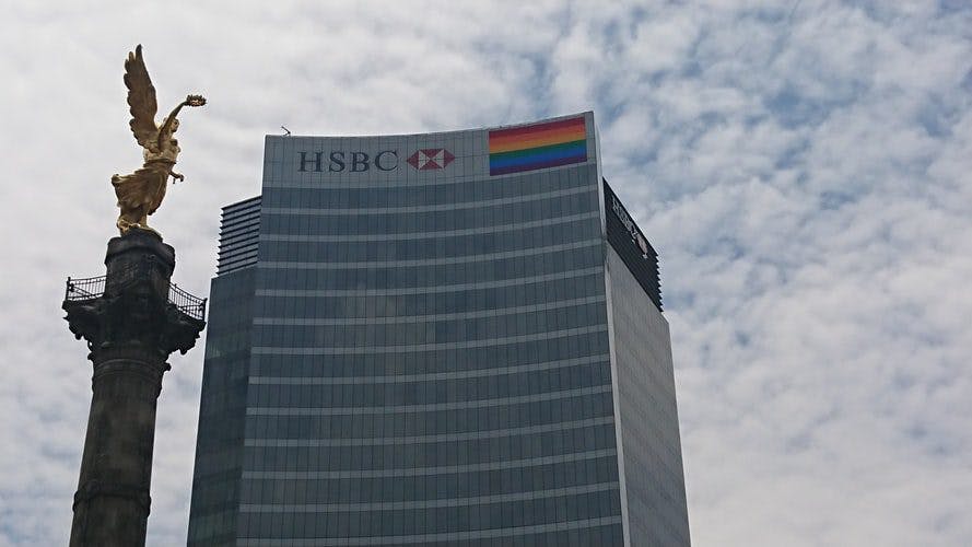 A tall building stands behind a statue of a rainbow flag, symbolizing diversity and inclusivity.