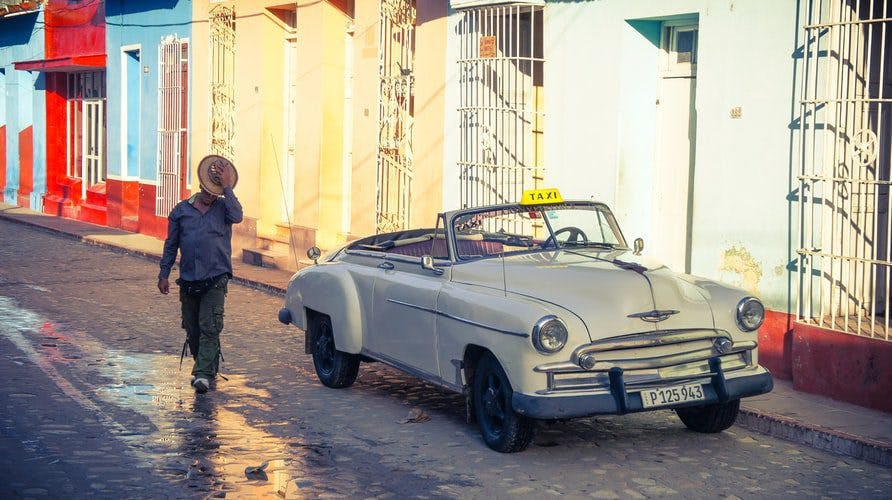 A person walking past an antique automobile on a cobbled street