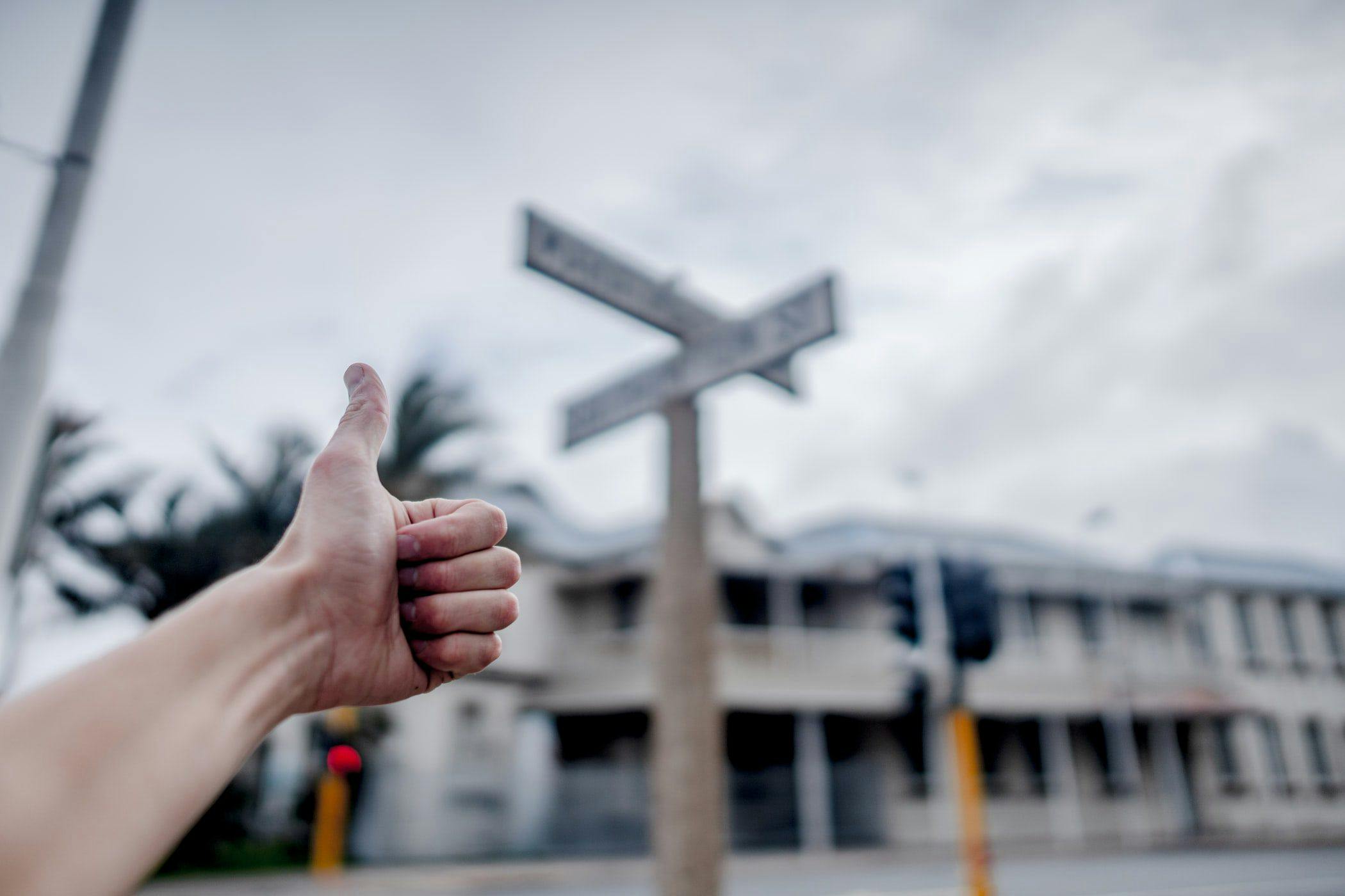 a hand giving a thumbs up in front of a street sign