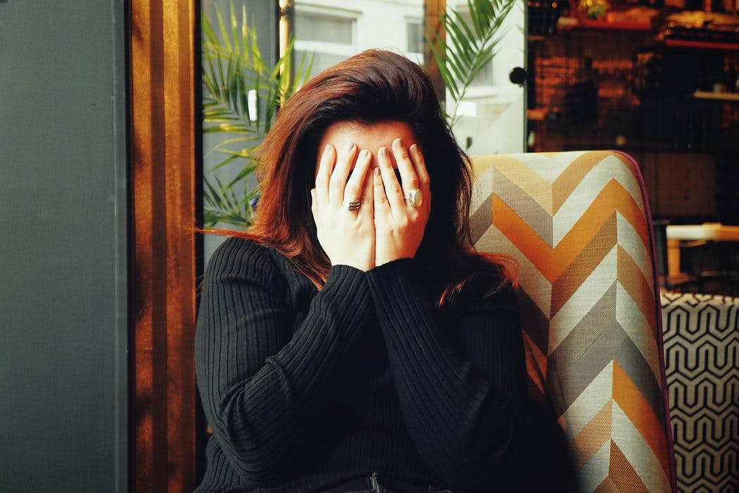 a woman sitting in a chair covering her face with her hands