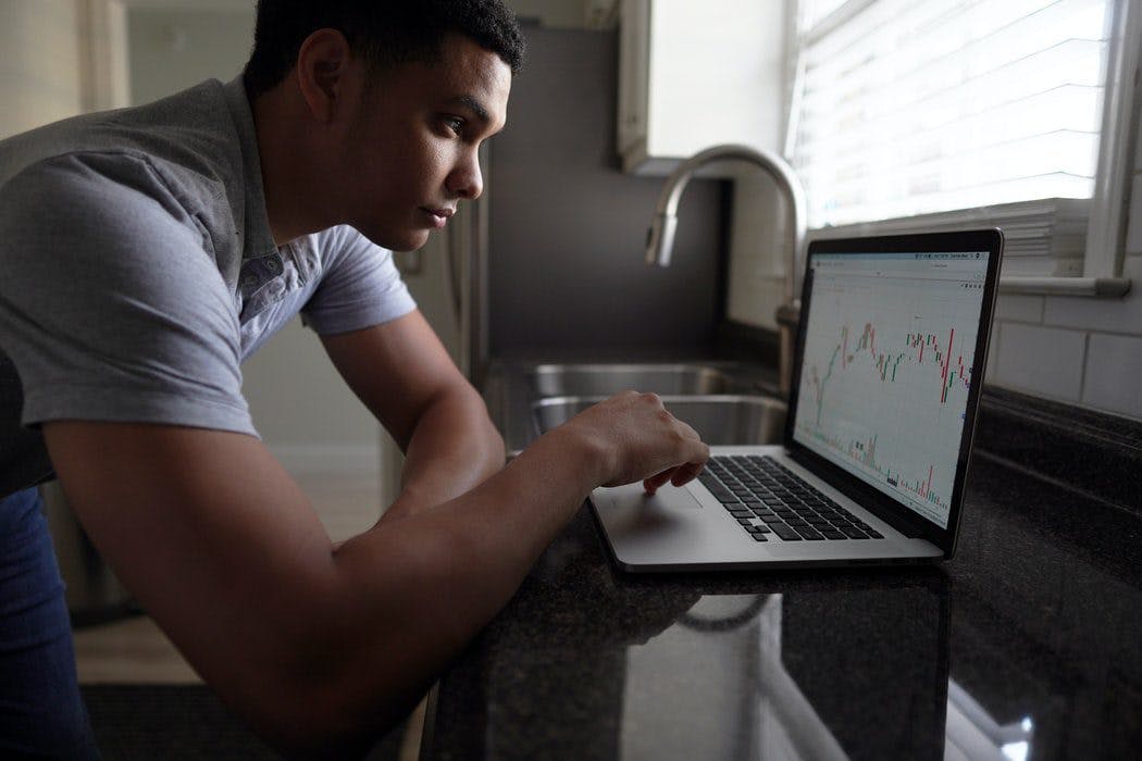 A man intently gazes at a laptop screen displaying a stock chart, analyzing market trends and financial data.
