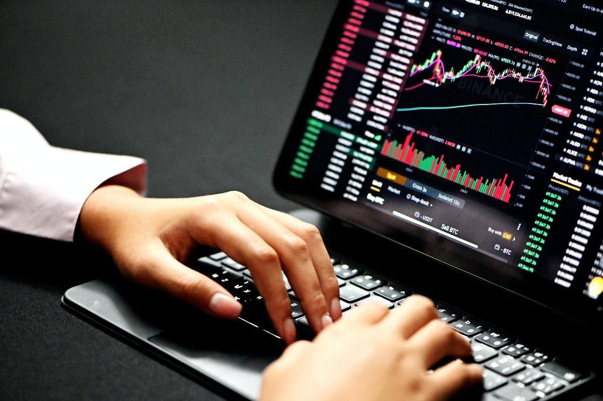 A person intently typing on a laptop, displaying stock market graphs.