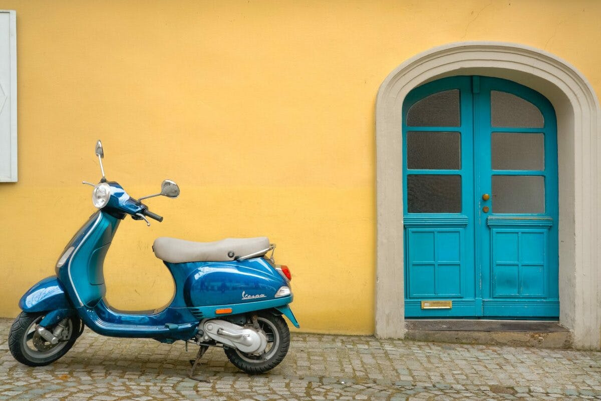 A parked blue scooter stands before a yellow building, creating a vibrant contrast between the two colors.
