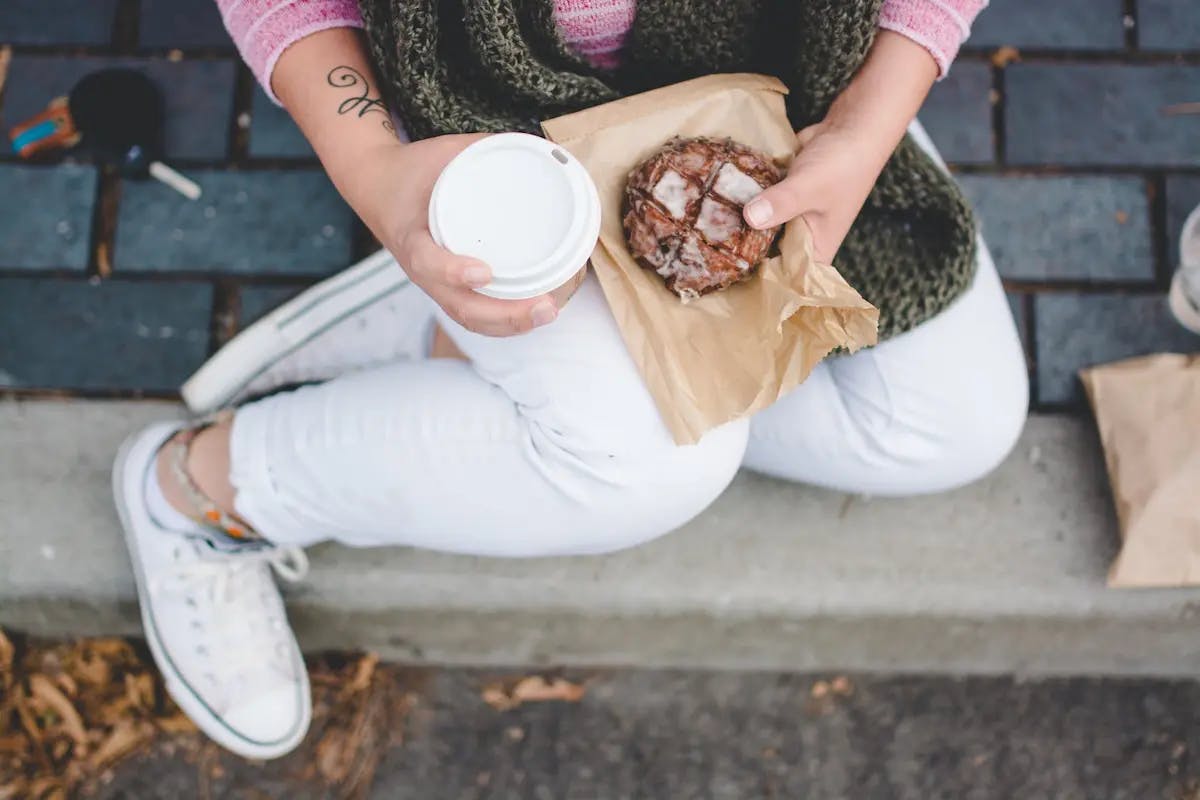 a girl sitting on a stone ledge holding a donut and a cup of coffee