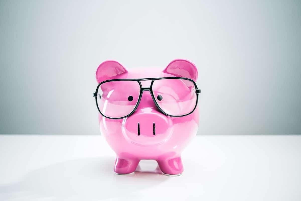 Pink piggy bank with glasses on white background.