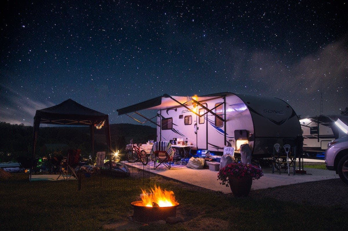 A camping trailer illuminated by starry night sky, offering a cozy retreat amidst nature's beauty.