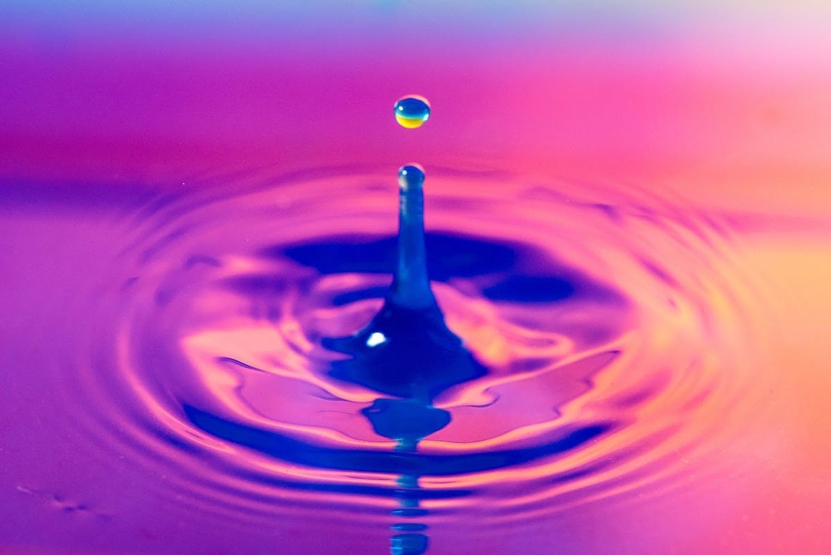 Colorful water droplet on vibrant rainbow backdrop.