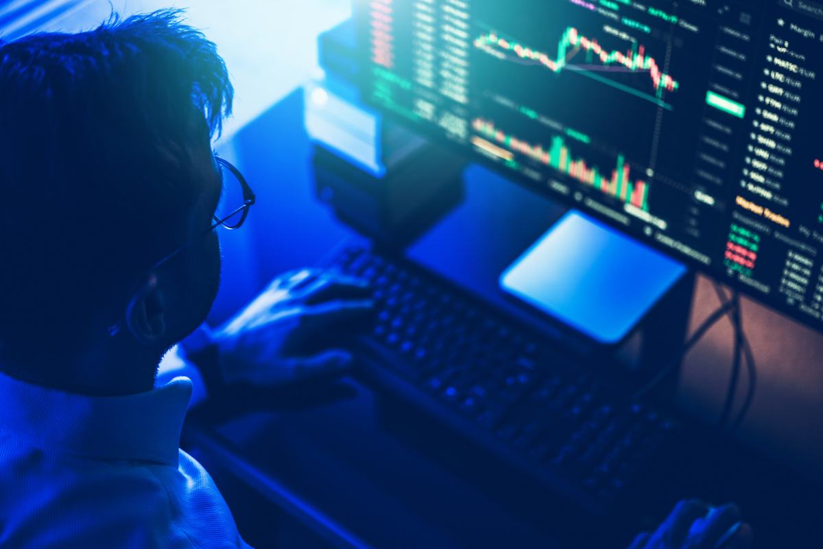 A man at a desk, looking at a computer screen displaying stock market information.