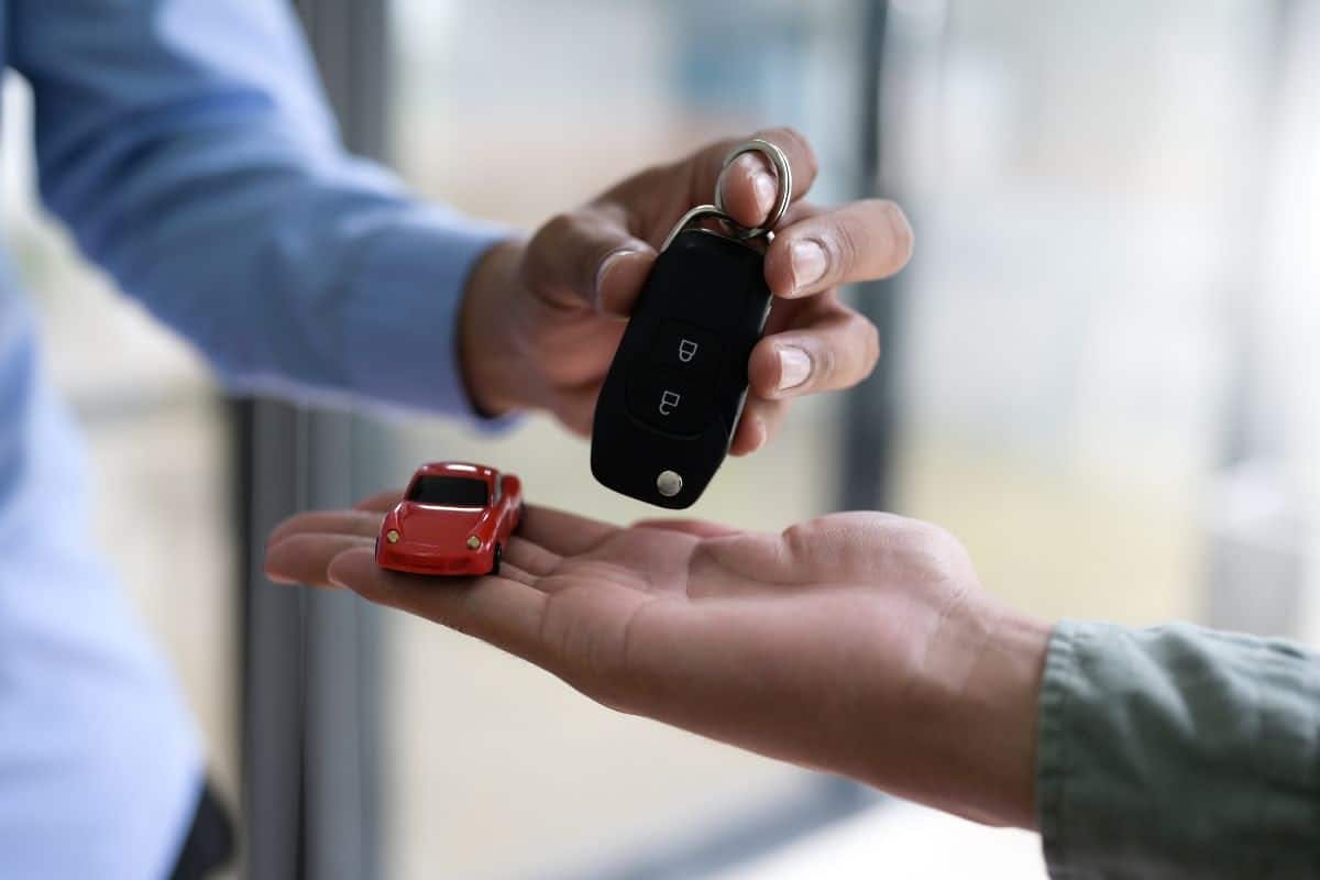 A man handing a car key to another person, symbolizing trust and transfer of ownership.