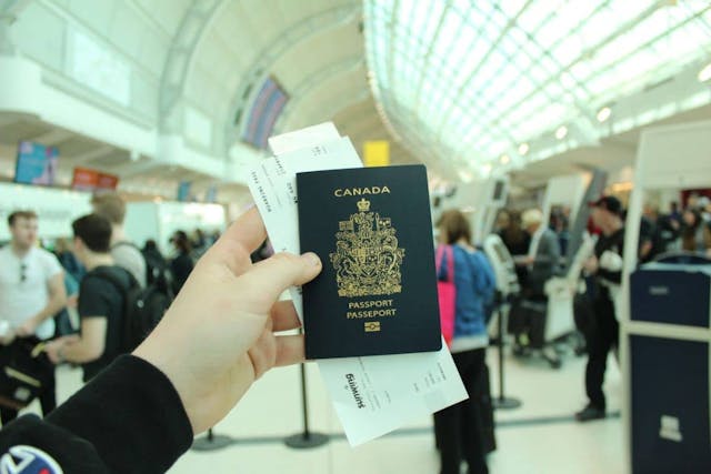 hand holding a Canadian passport and a plane ticket inside an airport