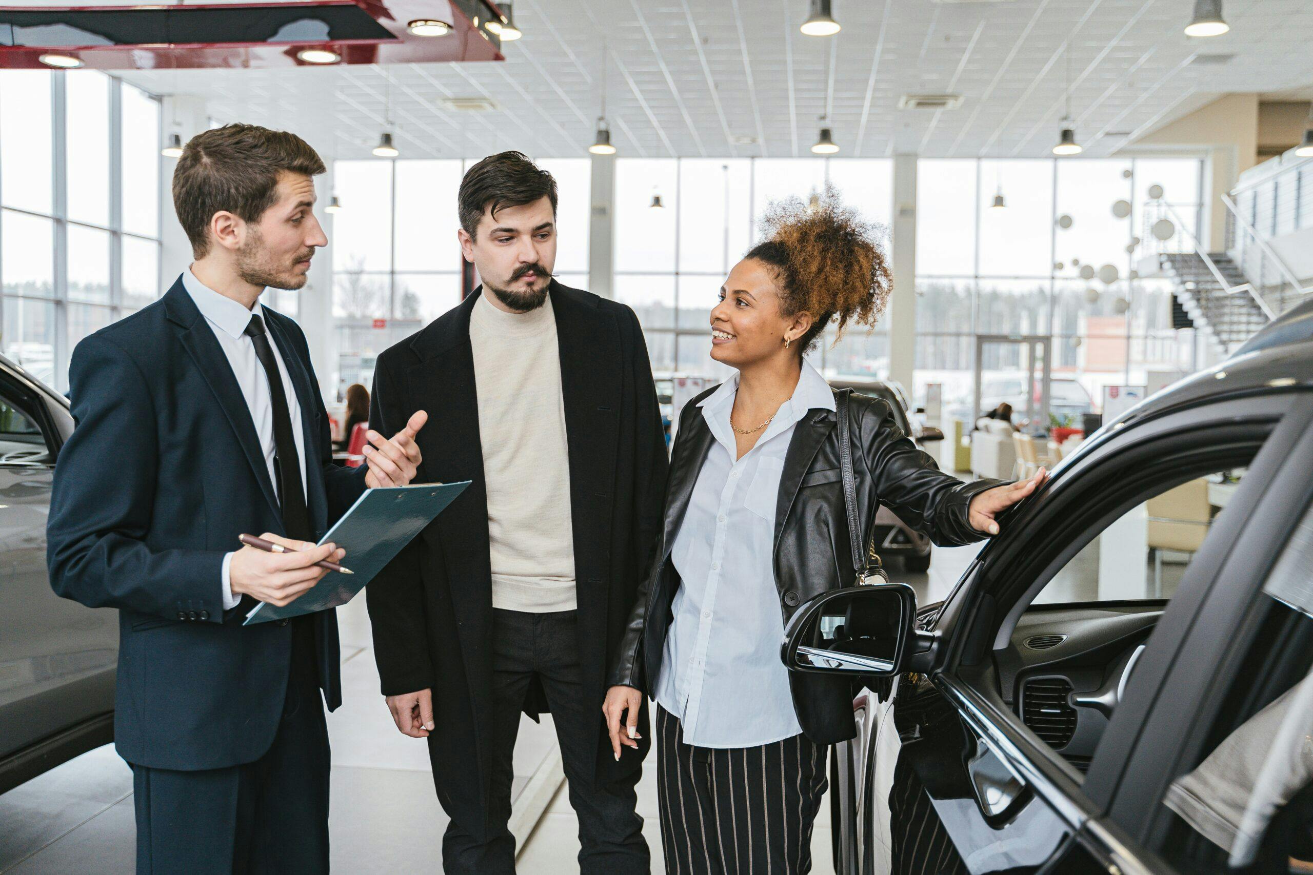 Two individuals and a lady inside an automobile dealership.