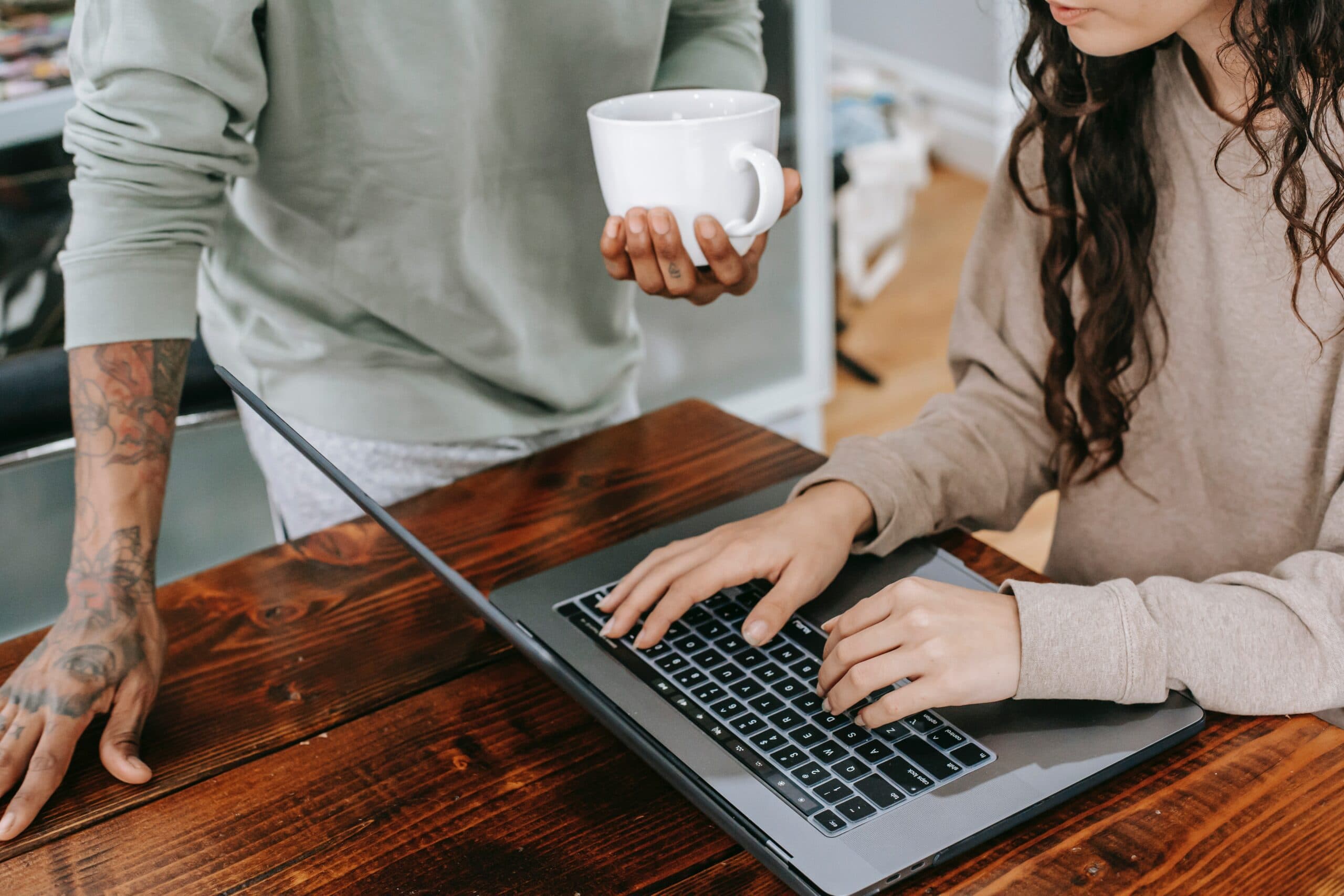 a person holding a cup and girl typing on a laptop